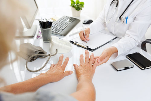 Old woman with arthritis showing her hands to female doctor